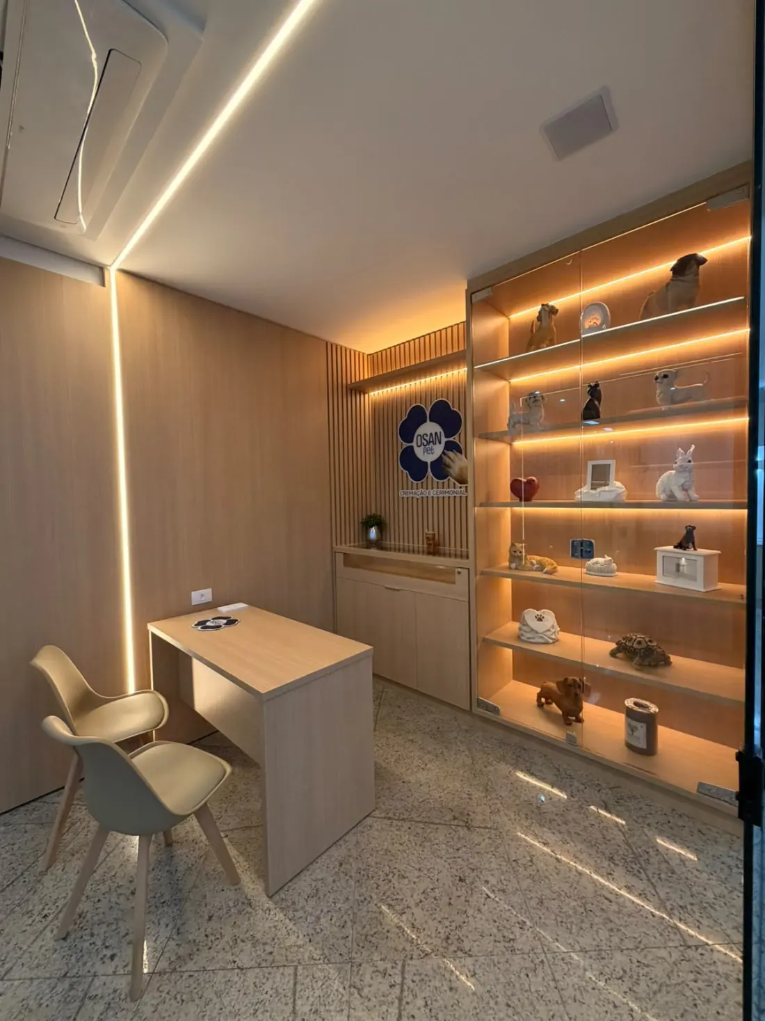 Sala de atendimento da OSAN Pet, com mesa, cadeiras e a vitrine iluminada de urnas
